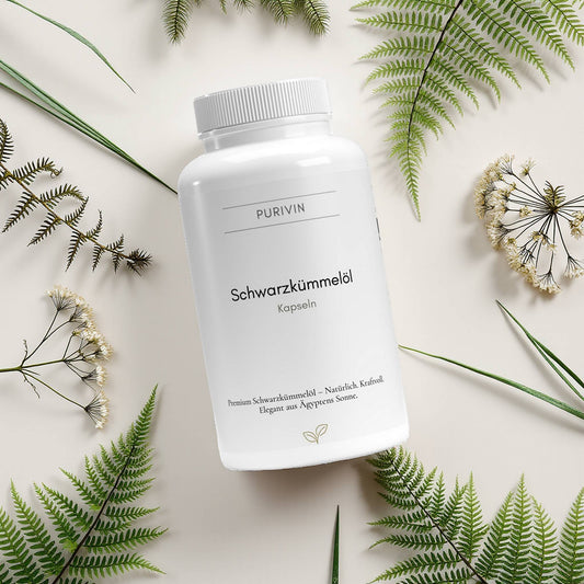 Purivin Schwarzkümmelöl Kapseln – natürliches Premiumöl aus ägyptischem Schwarzkümmel, auf hellem Hintergrund mit grünen Farnblättern und Blüten dekoriert